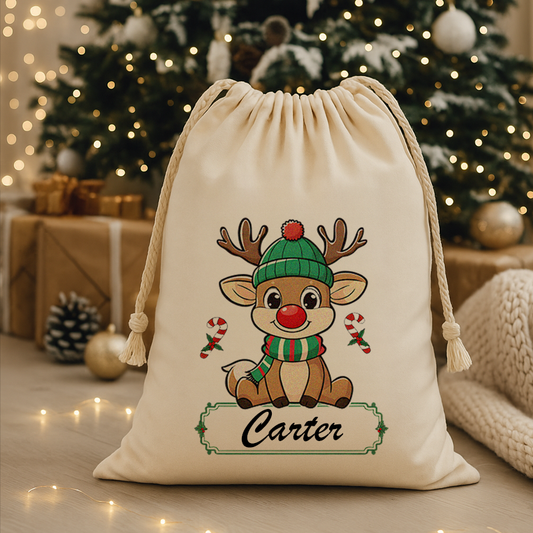 Personalized Christmas Santa sack with a cute boy reindeer design and the name “Carter,” placed in front of a decorated Christmas tree with warm lights, wrapped presents, pinecones, and cozy holiday décor.
