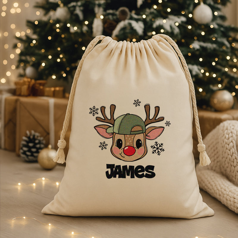 Beige drawstring bag with a reindeer design and 'CUSTOM' text, placed in front of a decorated Christmas tree.