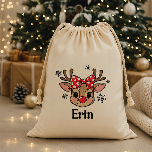 Drawstring bag with a reindeer design and 'CUSTOM' text, placed in front of a decorated Christmas tree.