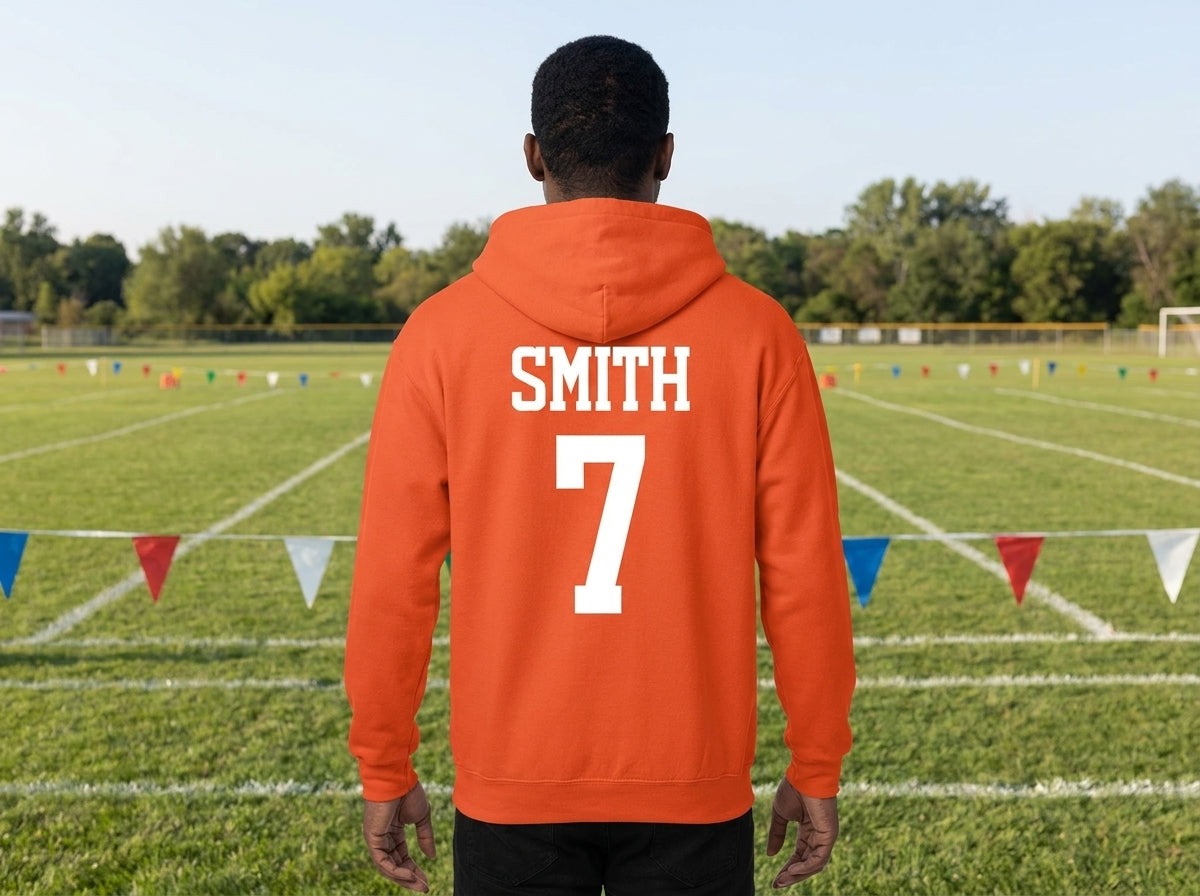 A person standing on a sports field, viewed from behind, wearing an orange hoodie with the name 'SMITH' and number '7' printed in white on the back.