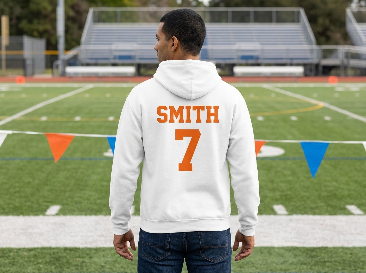 A man standing on a sports field, viewed from behind, wearing a white hoodie with 'SMITH' and the number '7' printed in orange on the back.