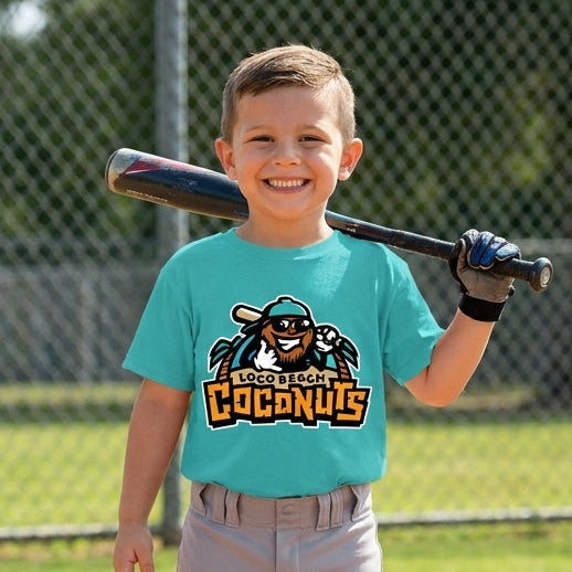 A young boy smiling on a baseball field wearing a bright turquoise t-shirt with a logo graphic, gray pants, and holding a bat over his shoulder.
